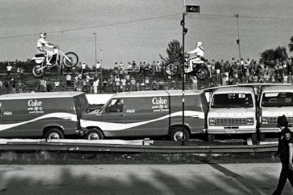 Evel Knievel doing a stunt of jumping over multiple Coke vans