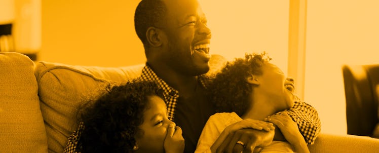 A dad with his two daughters who finished elementary school laughing on the couch while watching TV