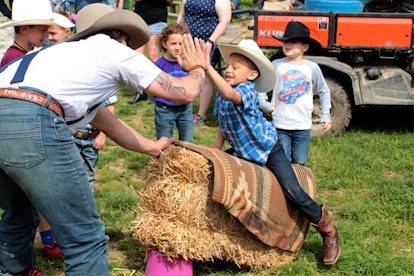 A little boy during a mutton busting simulation on a haystack