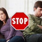 A married couple sitting on a couch with their backs to each other and a stop sign visible between t...