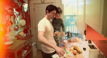 A dad in the kitchen preparing a meal while holding his toddler in his arms