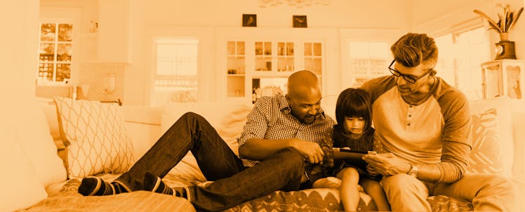 Two gay dads sitting together on a couch with their daughter