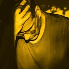 A man recovering from drug addiction sits in a chair with his head in his hand. Yellow color filter