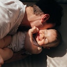 candid photo of a father kissing a laughing baby in bright afternoon light with high-contrast shadow...