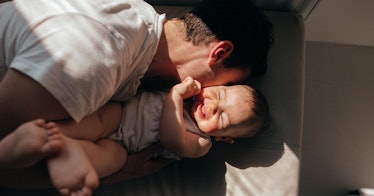 candid photo of a father kissing a laughing baby in bright afternoon light with high-contrast shadow...