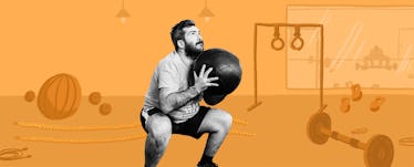 A man squats with a medicine ball with gym equipment in the background