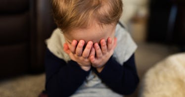 An embarrassed child buries their face in their hands.