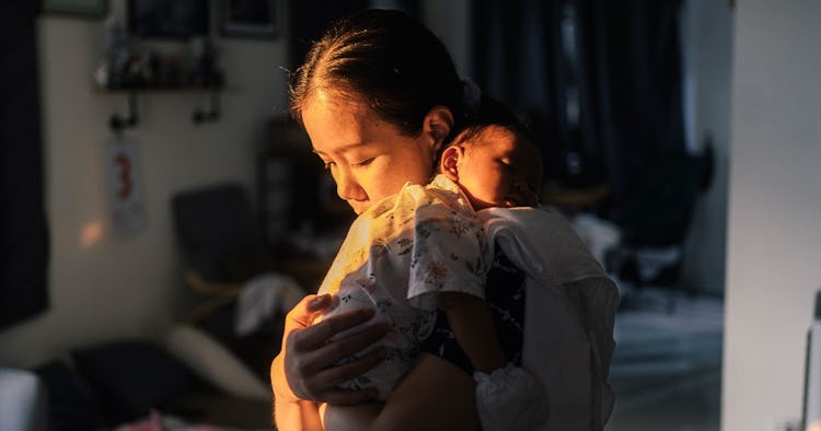 Mother lovingly holding newborn baby while it falls asleep on her shoulder.