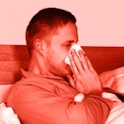 A man semi-lying in his bed wiping his nose with an orange color filter