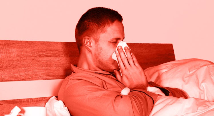 A man semi-lying in his bed wiping his nose with a tissue