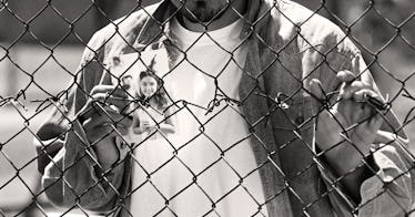 A father standing behind a fence in jail, holding a photo of his daughter