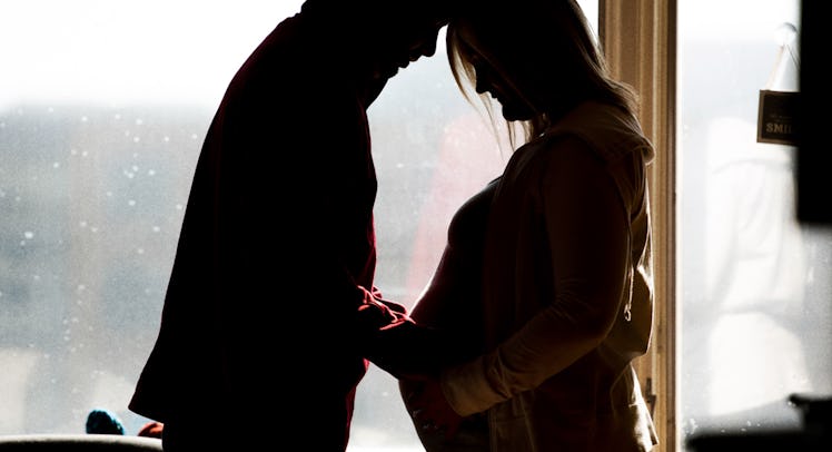 silhouette of a man placing a hand on the baby bump of his pregnant wife