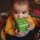 Baby chewing on a large toy block.