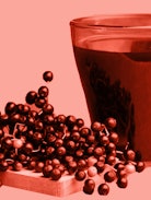 sepia edit of a cup of black elderberry syrup placed beside some elderberries on a wooden board