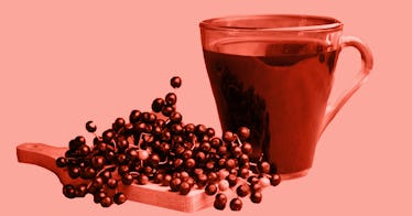 sepia edit of a cup of black elderberry syrup placed beside some elderberries on a wooden board