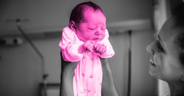 A newborn baby being held appears to strain while pooping
