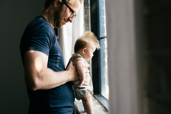 A Swedish dad in a blue shirt holding his son in front of a window with both of them looking out