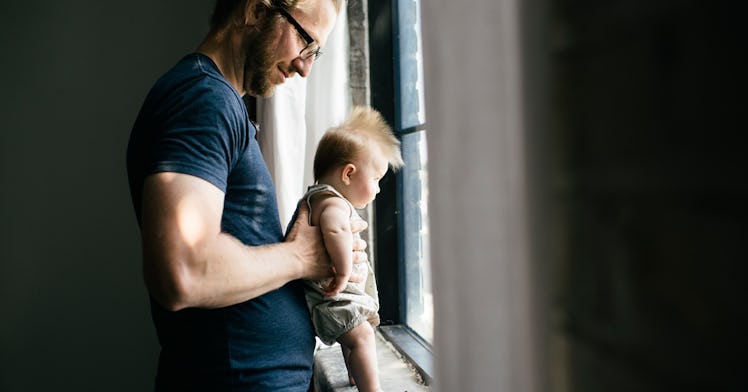 A Swedish dad in a blue shirt holding his son in front of a window with both of them looking out