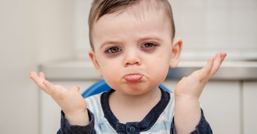 Frowning 4 year old boy with dark circles under his eyes lifting his hands in a questioning way