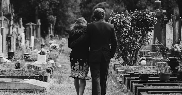 greyscale edit of man dressed in a suit with arm around a woman in a black dress walking through a c...