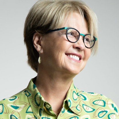 Anne Collier in a light green silk shirt with geometric patterns and glasses. She's smiling and look...