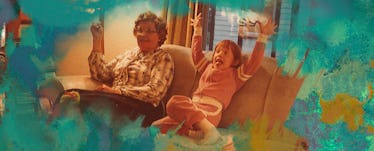 An annoying child sits on the couch with a parent, their hands raised in the air.