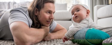 A father lying stomach down on the floor next to his baby daughter