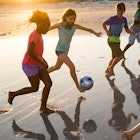 5 kids playing football on a sand beach