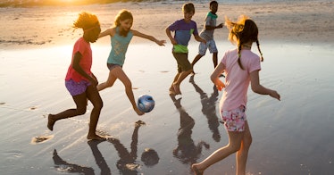 Five kids playing soccer on a sand beach