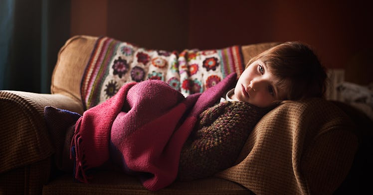 A sick girl laying on a couch under blankets.