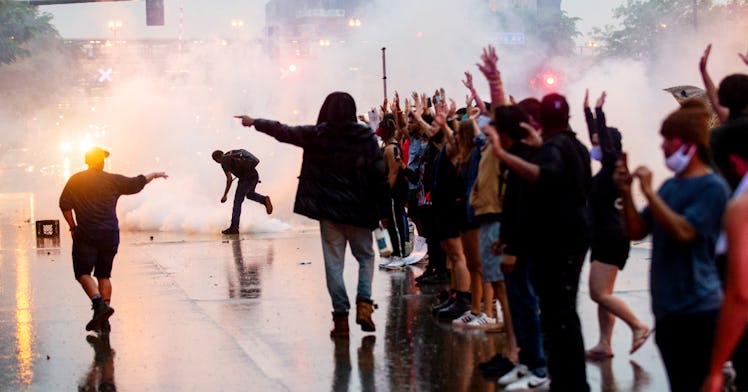 A crowd of people holding hands in the air as tear gas is fired behind them