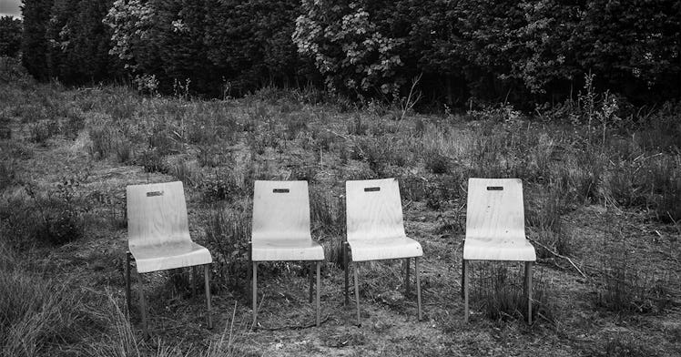 Four wooden school chairs standing empty in an overgrown field