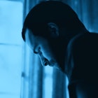 A depressed father stands in front of a window looking out. A dark blue color filter
