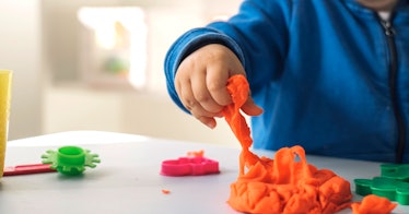 toddler in blue hoodie pulling on a orange string of play dough - a sensory activity for 1 year olds