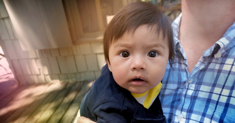 A baby in their dad's arms stares at the viewer.