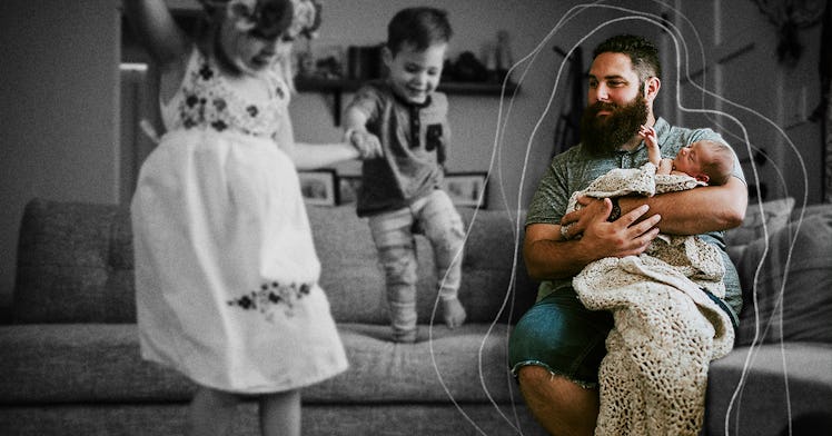 A dad on the couch holding his newborn baby while his two toddlers jump around them