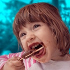A toddler eating a popsicle and making a mess in front of a background of a blue tinted forest