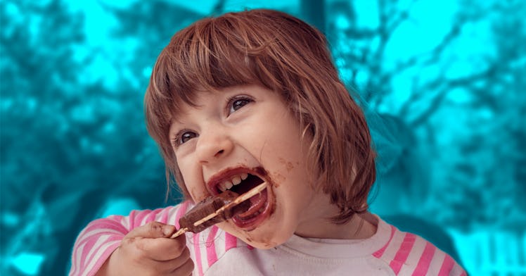 A toddler eating a popsicle and making a mess in front of a background of a blue tinted forest