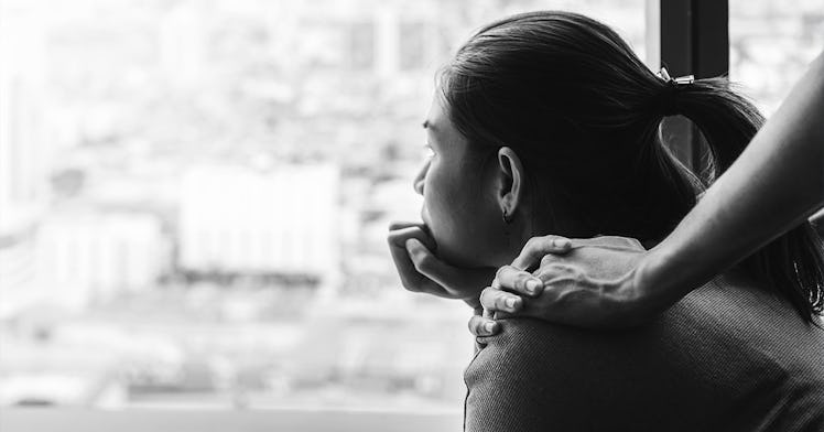 A woman, in black and white, looks out a window, with a hand on her shoulder