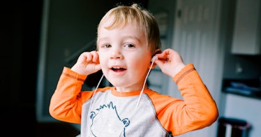Blonde 4 year old boy in white shirt with orange sleeves smiling and putting earbuds in to listen to...