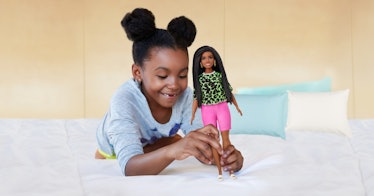 A little girl plays with a Barbie doll on her bed