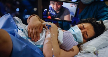A woman with a mask who has just given birth to her baby and her other son looking at her on a video...