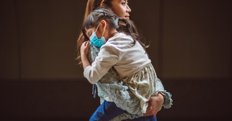 A mom holds her child, both in masks