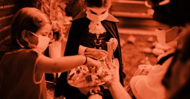 A group of three children take candy out of a bucket for halloween, wearing costumes and face masks....