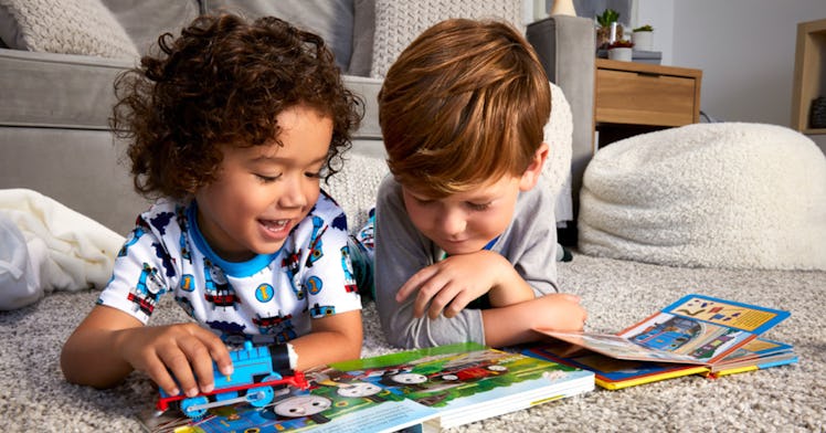 Two young boys play with a Thomas the Tank Engine toy while reading a Thoomas & Friends book
