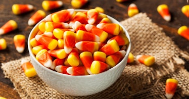 A bowl of candy corn placed on a woven cloth on a table 