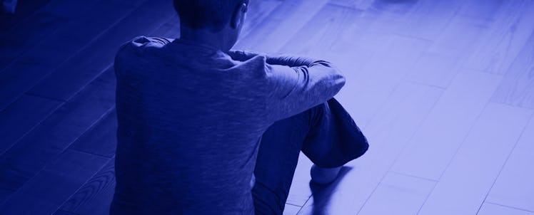 A man sitting on the floor in an empty room with his back turned trying to cope with stress
