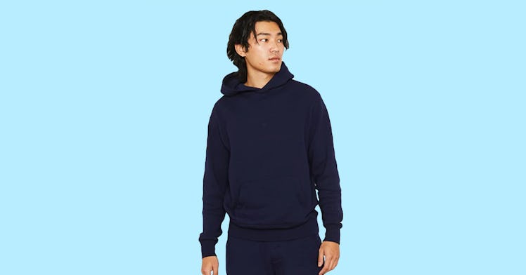 A model wearing Entireworld clothing, sweats and a hoodie, set against an aqua background