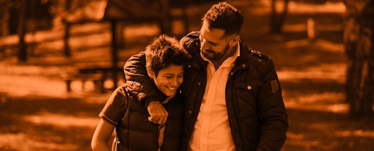 father with arm around son orange background