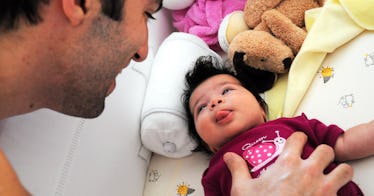 dad looking down at baby with black hair and pink shirt sticking her tongue out